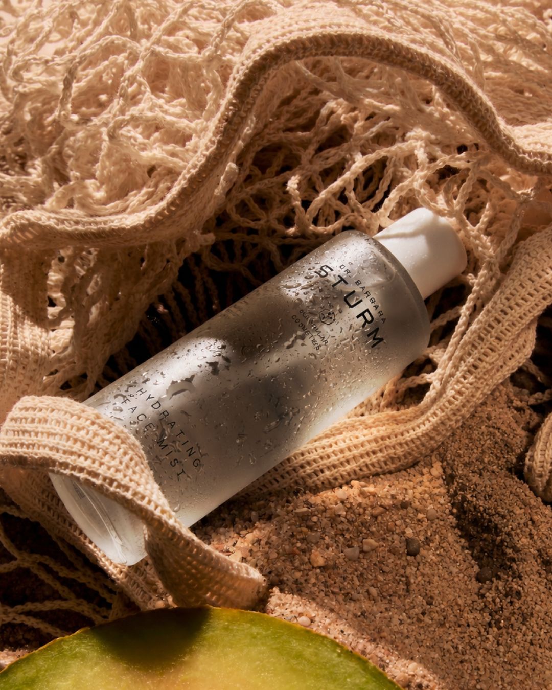 Clear bottle of skincare product on sandy surface, wrapped in netting.