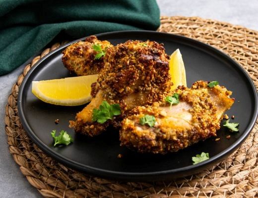 Crispy fried chicken pieces with lemon wedges and herbs on a black plate.