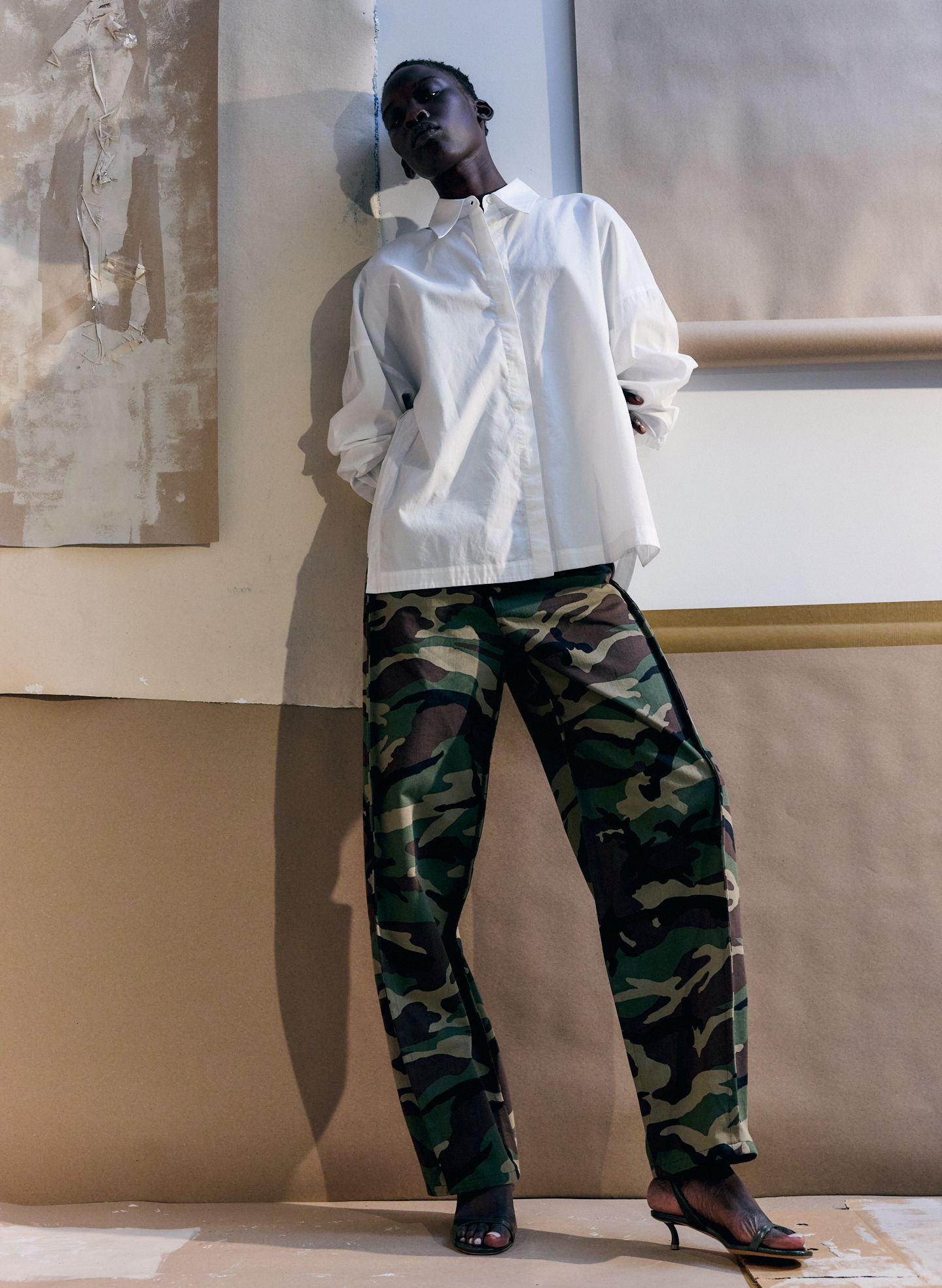 A model wearing a white shirt and camouflage pants in an artistic setting.