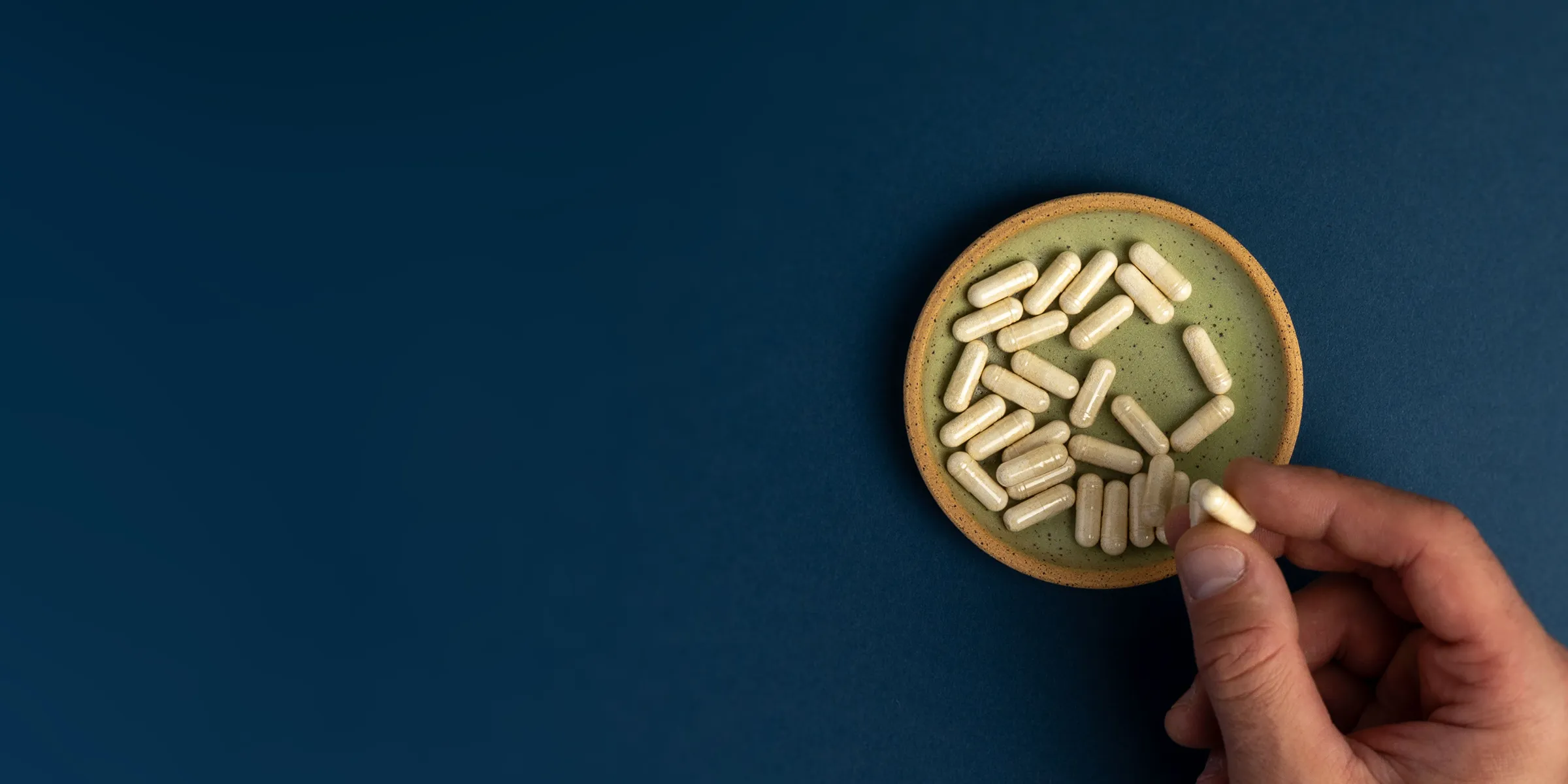 A shallow green bowl with a couple dozen Neuralli MP capsules in the bottom. A hand is grabbing one of the capsules.