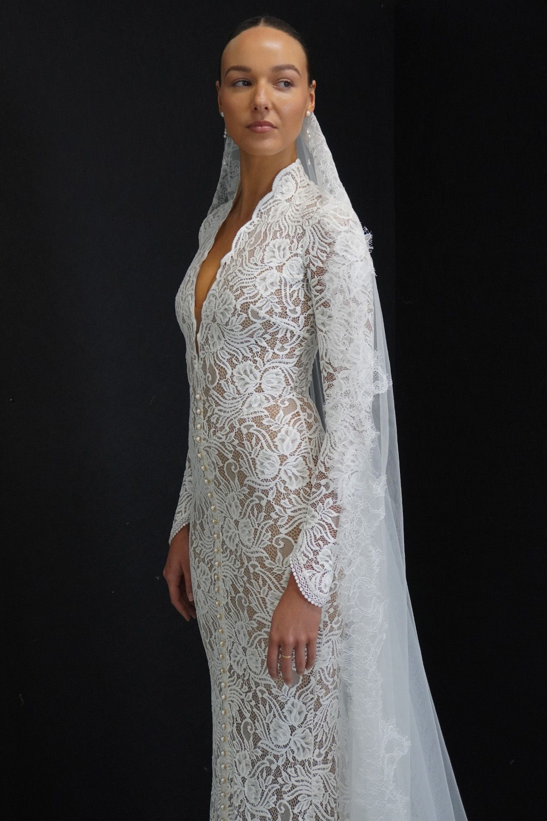 Model in a lace wedding dress with a veil against a dark background.