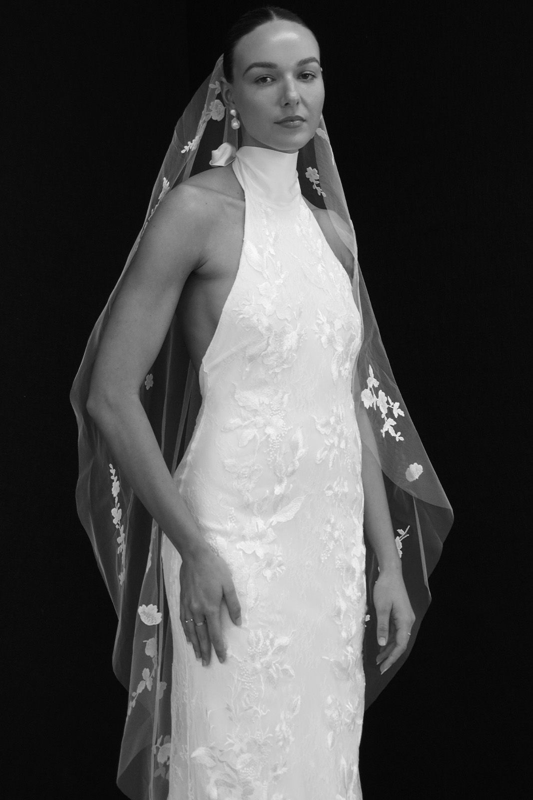 A model in a white wedding dress with a veil against a black background.