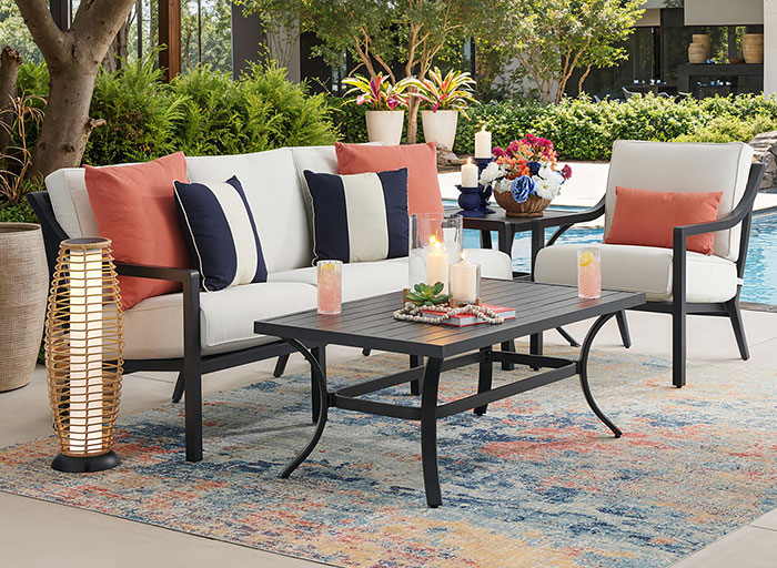 Outdoor seating area with cushions, table, and decorative elements near a pool.