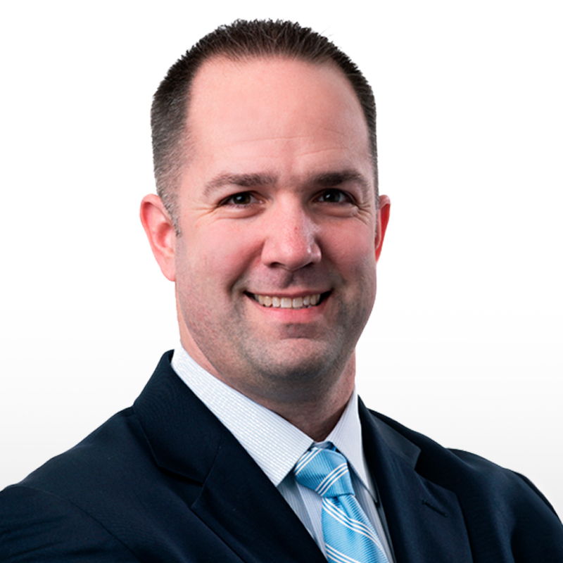 Man in a suit with a light blue tie, smiling against a white background.