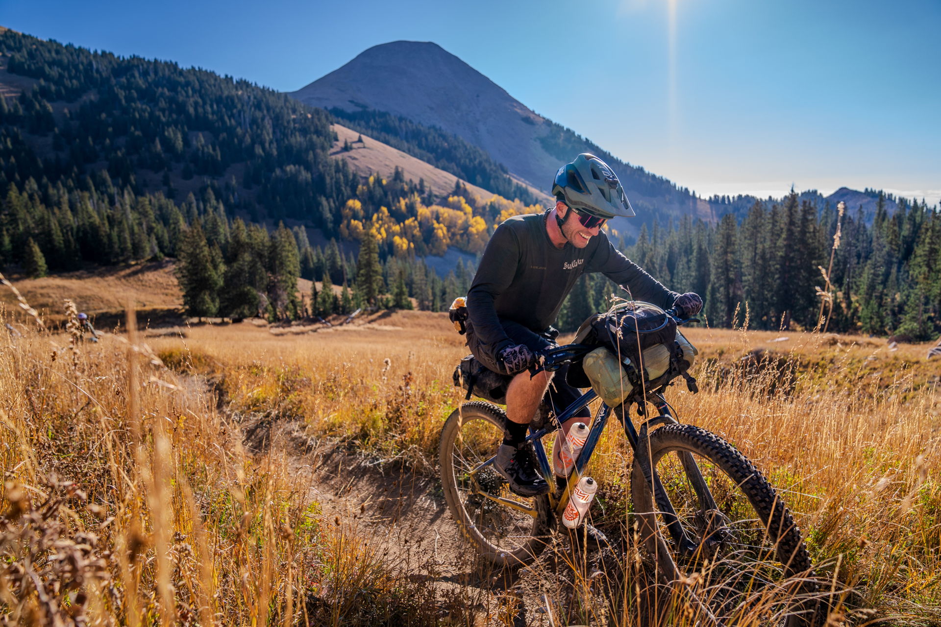 Biker navigating a trail with mountains and trees in the background.