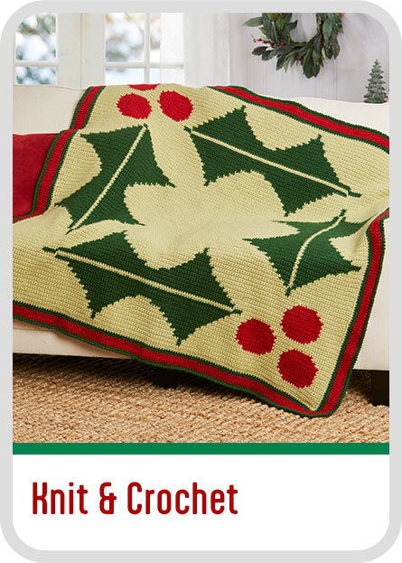 A knitted blanket with holly leaves and red berries on a couch. Christmas Knit and Crochet Kits