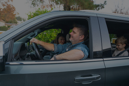 Man driving a car with two passengers inside.