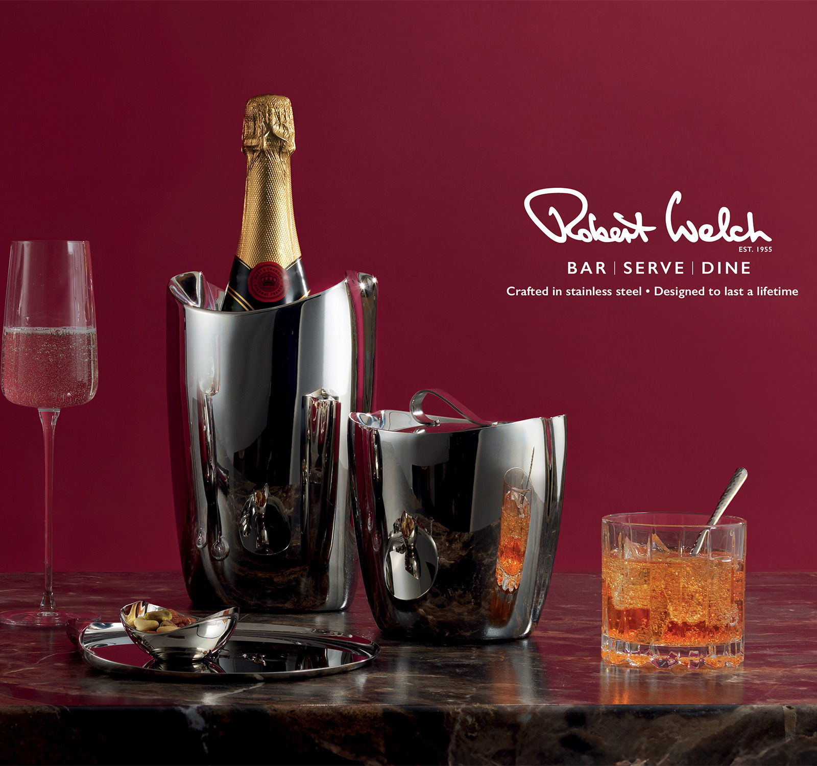 Champagne bottle in ice bucket with glasses and cocktail on a table.