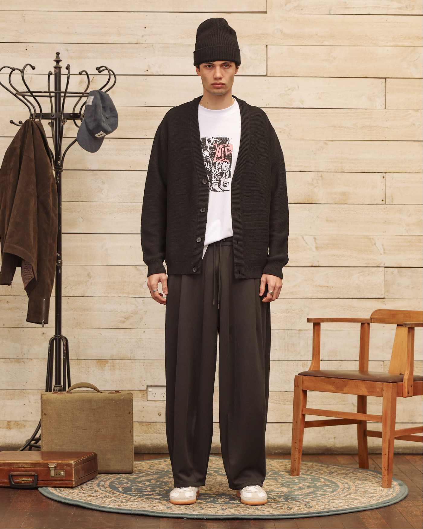 Man in casual outfit standing in a room with wooden walls and furniture.