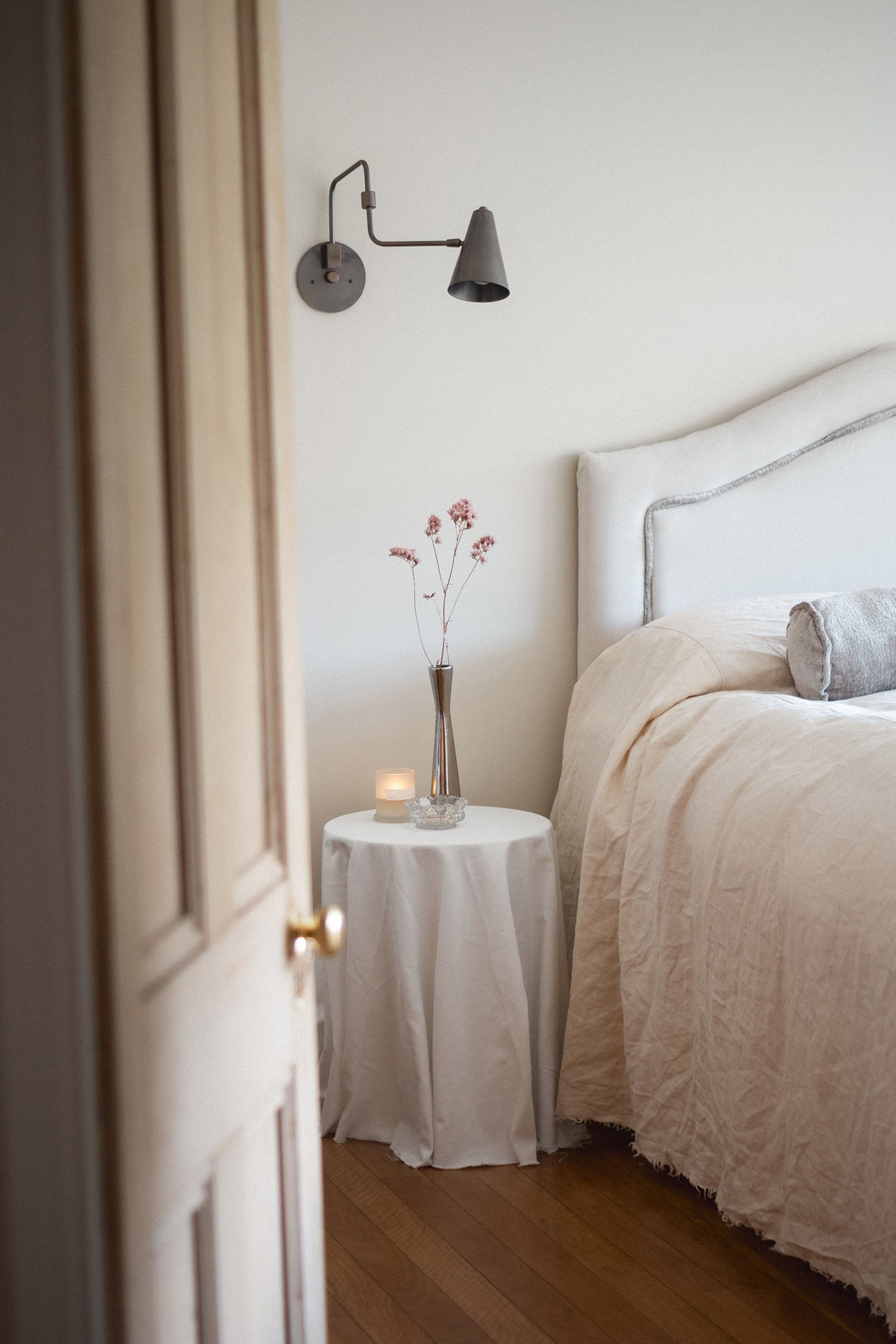 Cozy bedroom with a bed, lamp, and a vase of flowers on a table.
