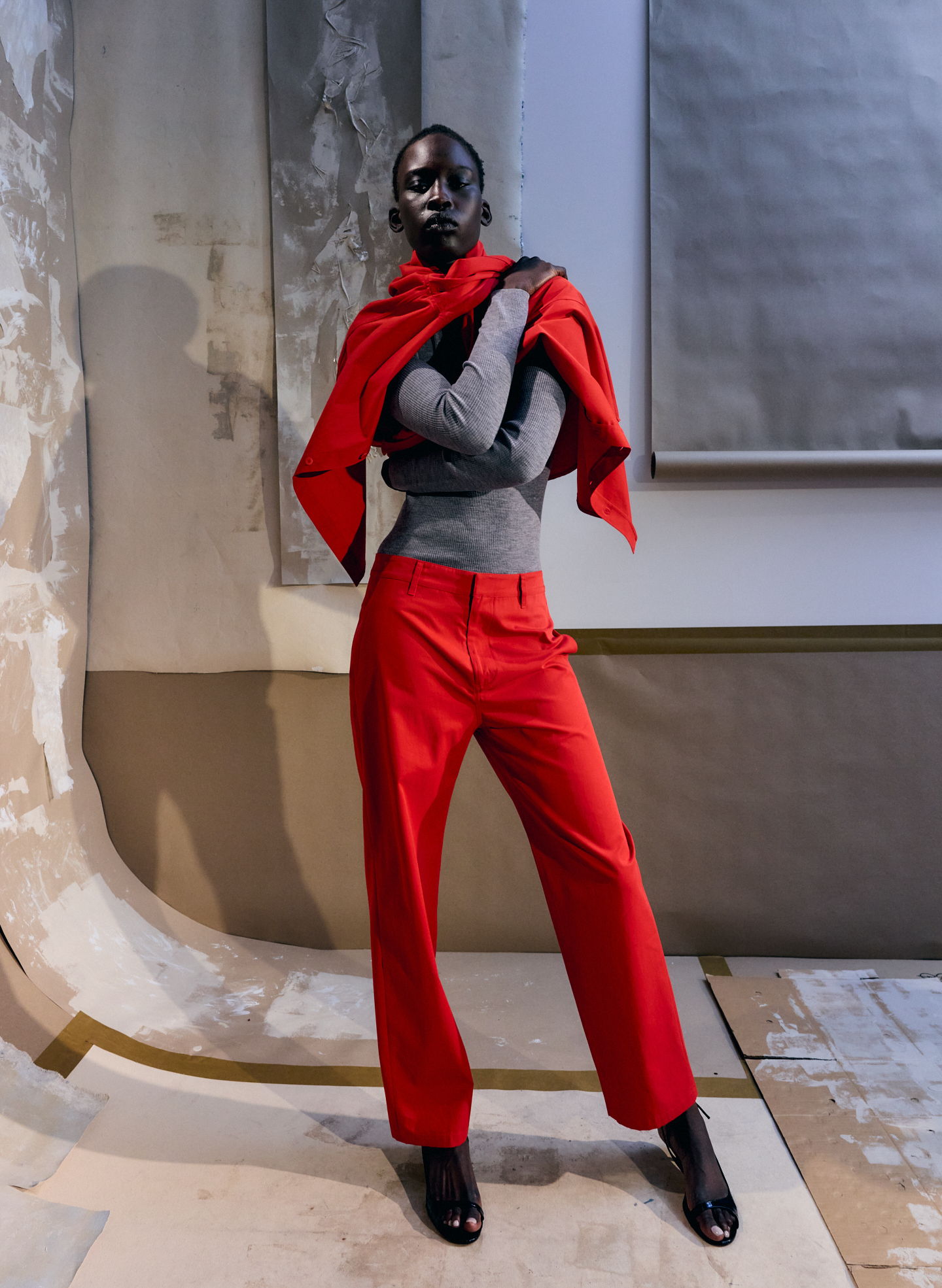 Model wearing a red scarf, gray top, and red pants in a studio setting.