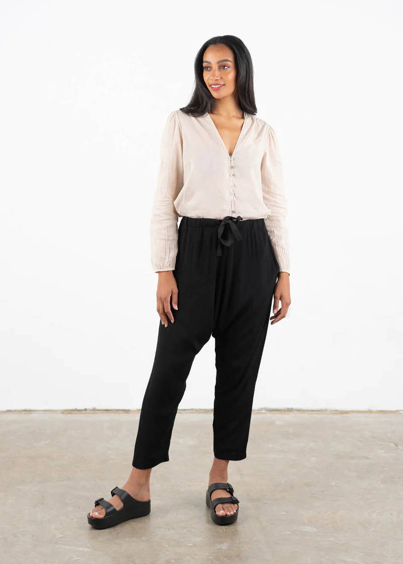 A model wearing a pair of black, cropped drop crotch trousers white a white long sleeved off blouse