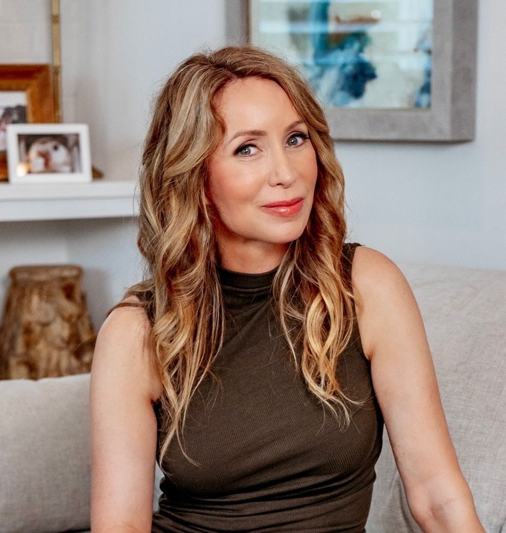 Woman with wavy hair sitting on a couch in a cozy living room.