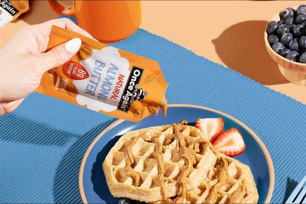 Hand pouring syrup over a waffle with strawberries and blueberries on the side.