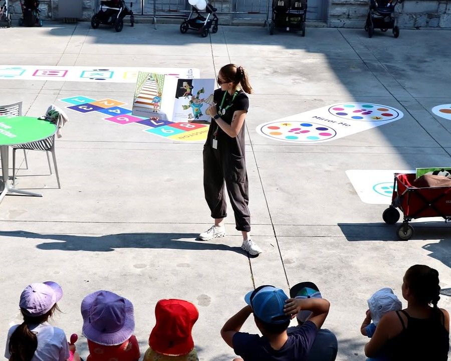 Person reading to children outdoors with colorful play area and seating.