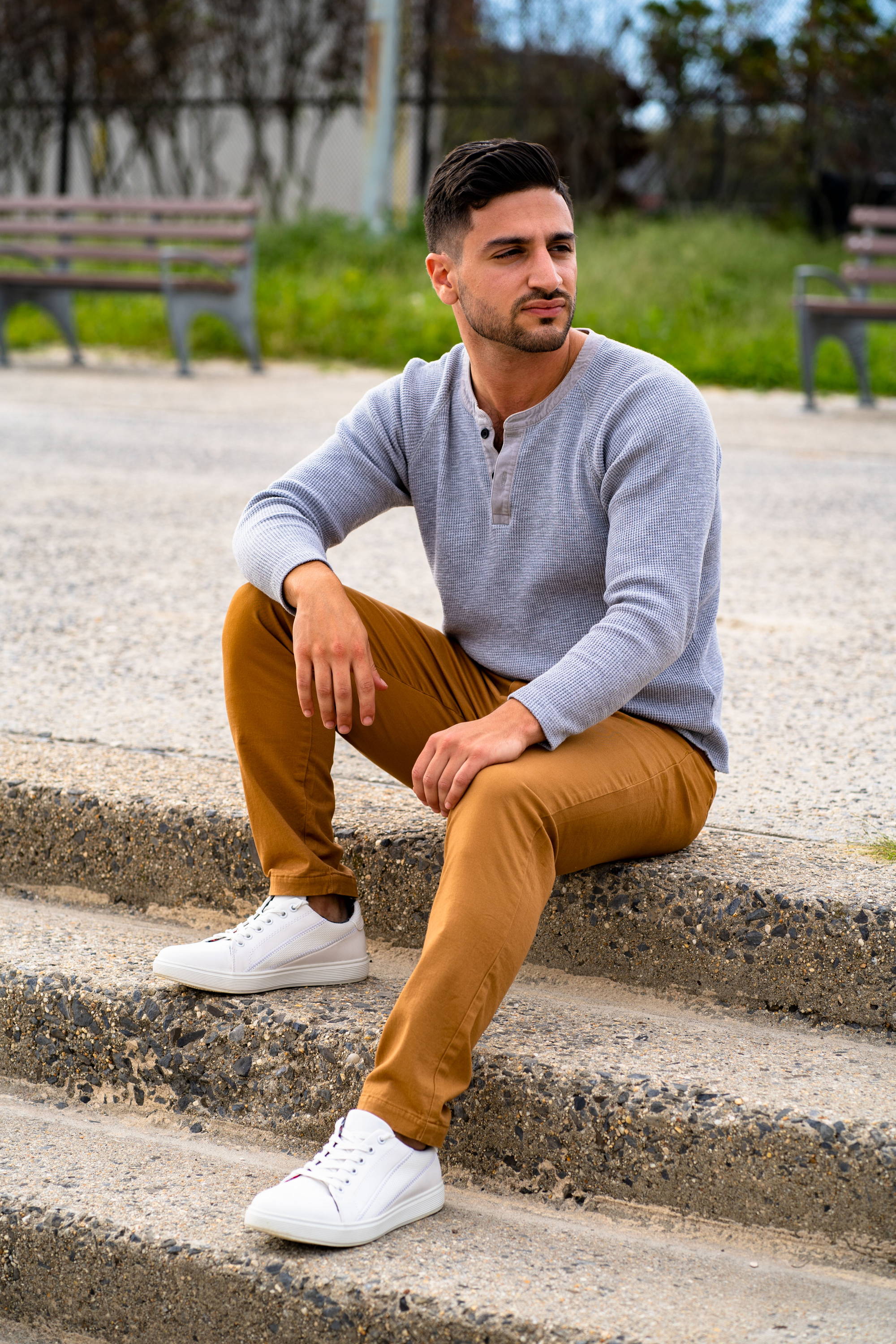 Male Model sitting on steps wearing white shoes, a gray henley, and chinos pants from under510.com