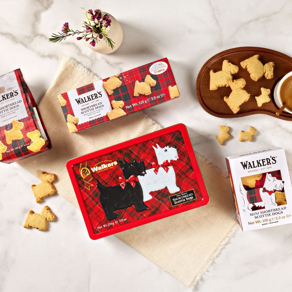 Assorted dog-shaped cookies in decorative packaging on a marble surface.