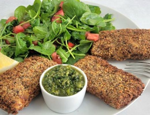 Breaded fish fillets with salad and green sauce on a plate.