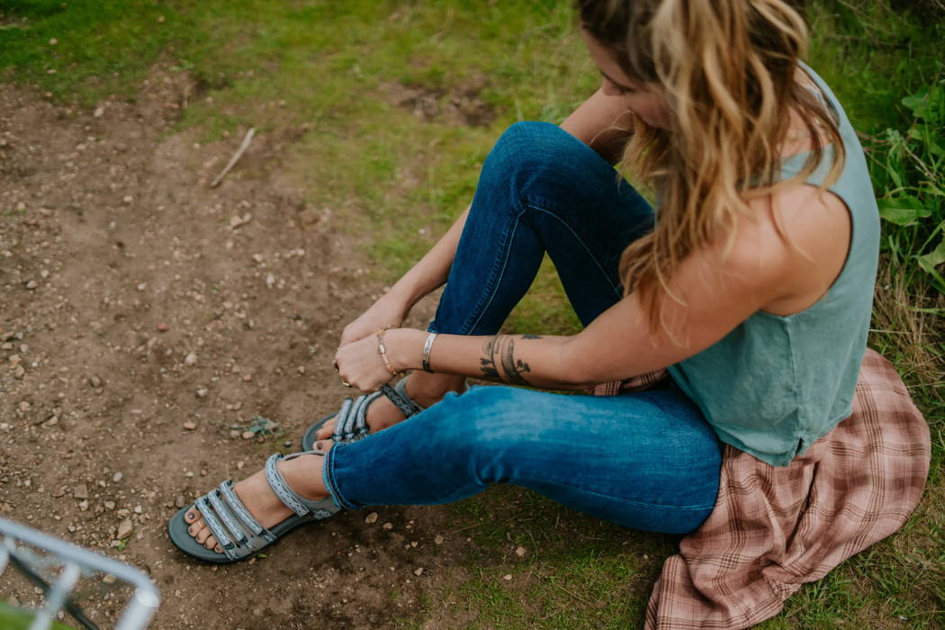 women fixing her hiking sandals while sitting on the ground