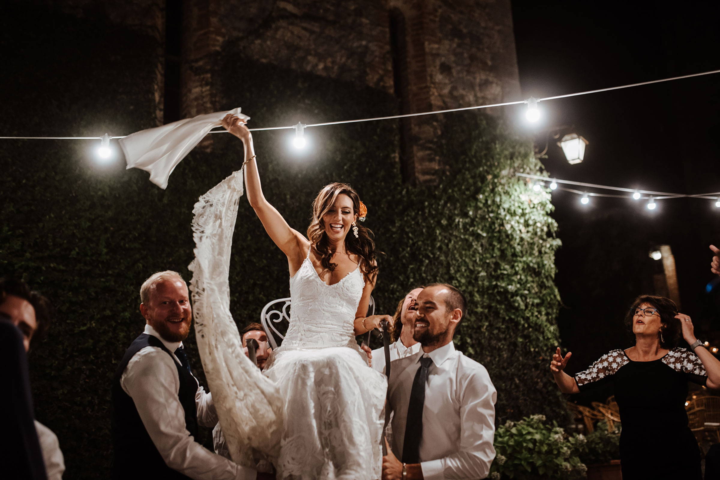 Bride wearing white dress being lifted on a chair by groomsmen