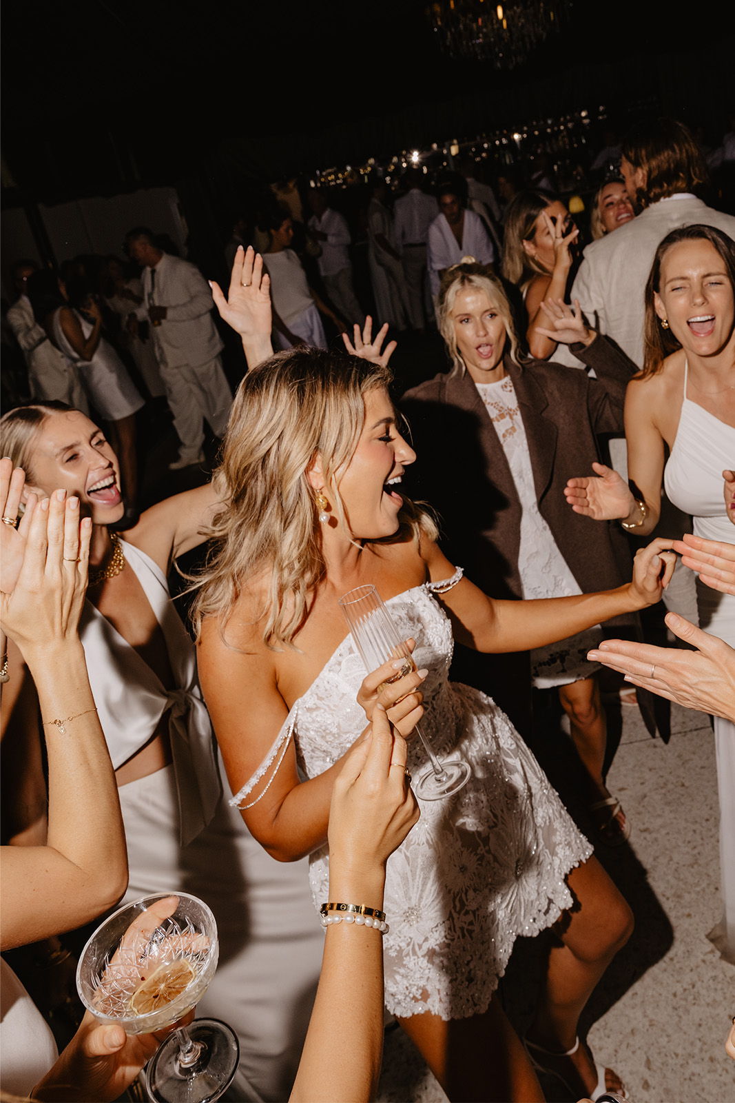 Group of women dancing joyfully at a celebration, wearing white outfits.