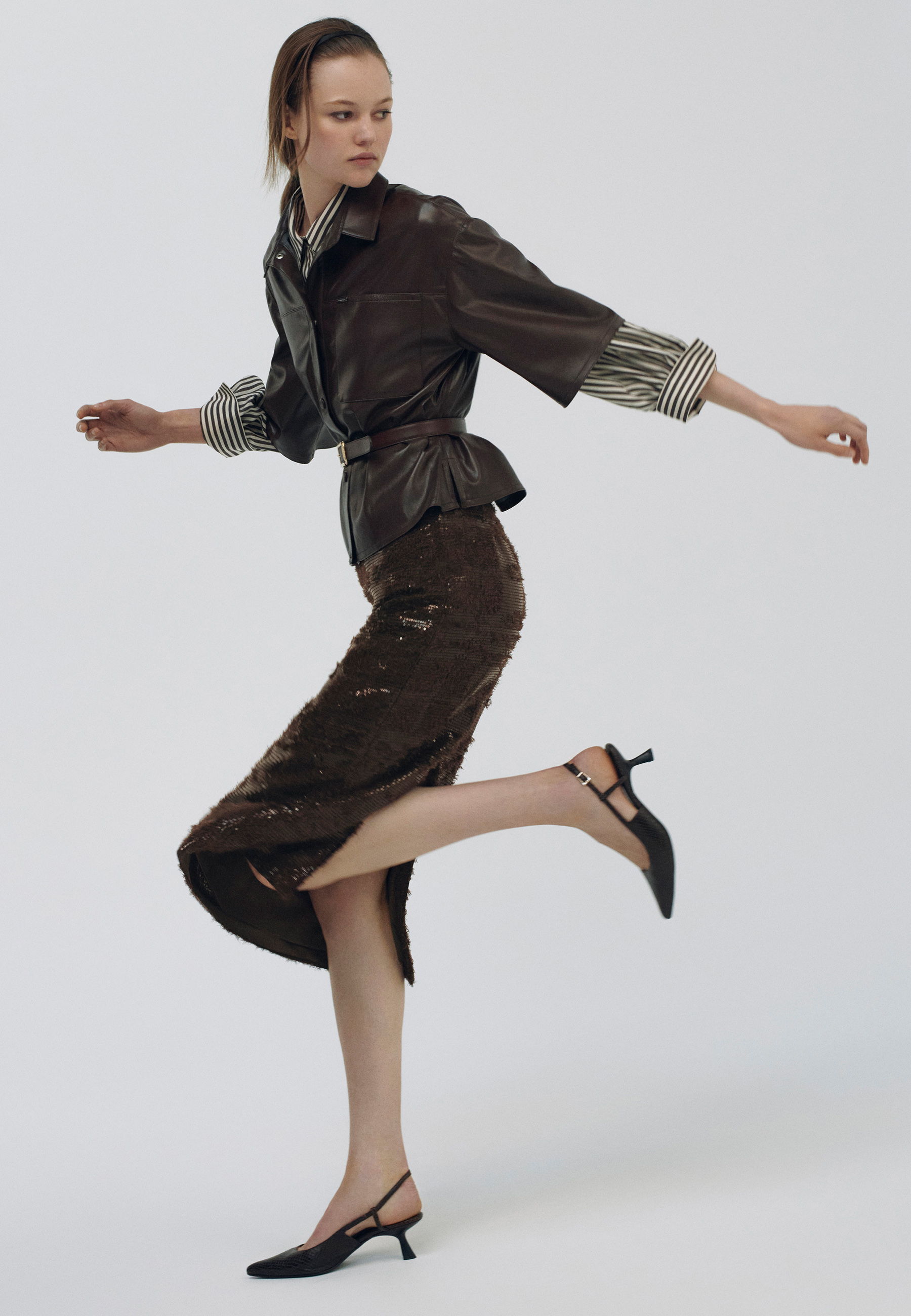 Model wearing a stylish brown outfit and black heels, posing dynamically.