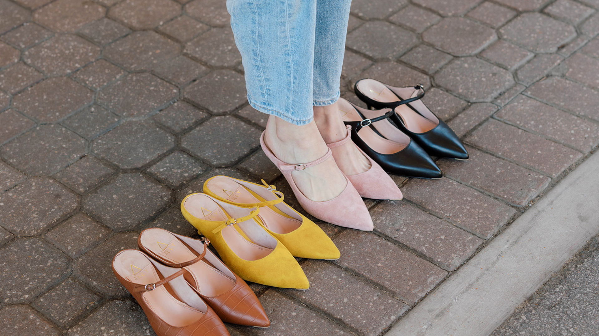 Person wearing jeans next to various colored pointed-toe shoes.