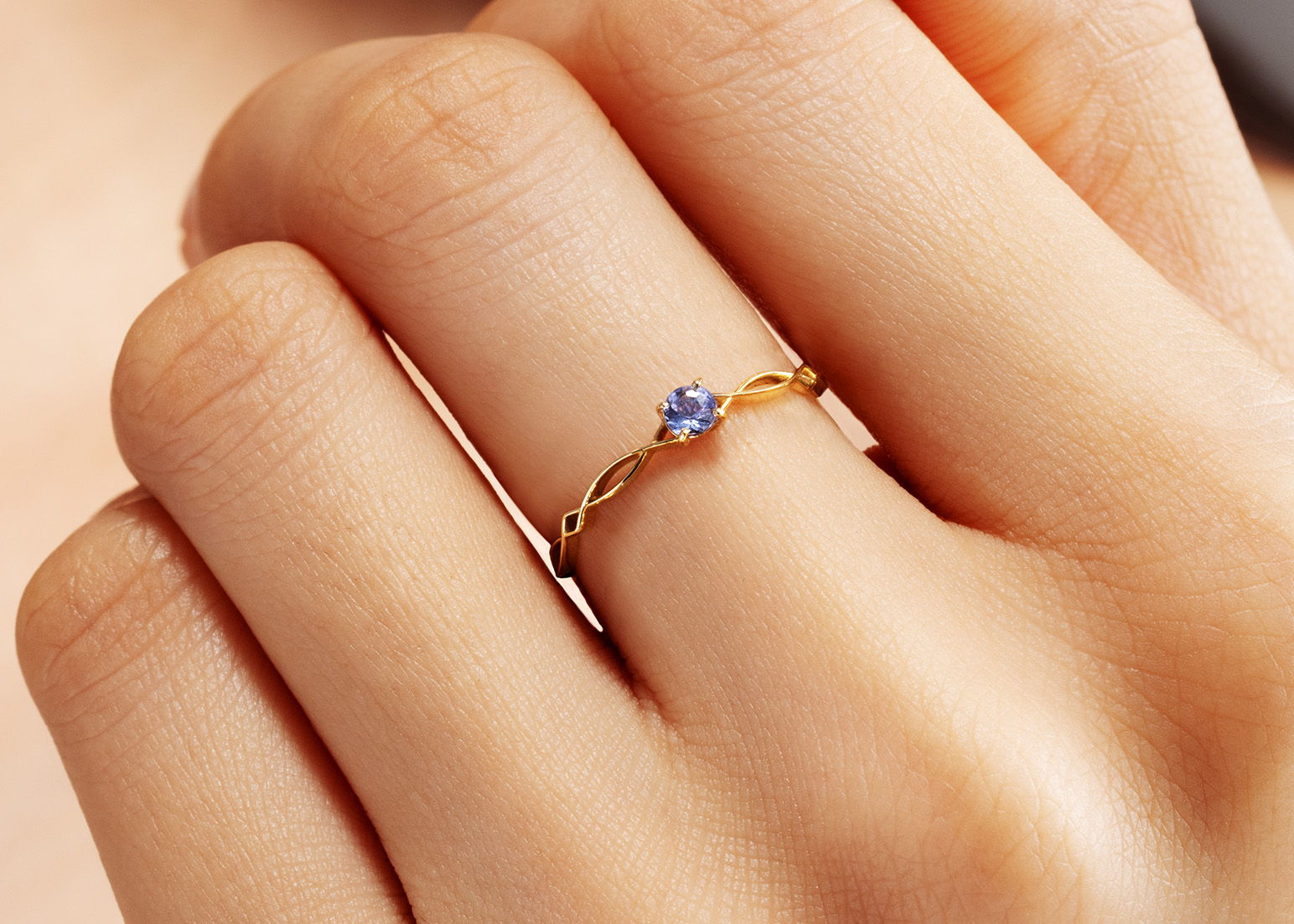A hand wearing a delicate gold ring with a small blue gemstone.