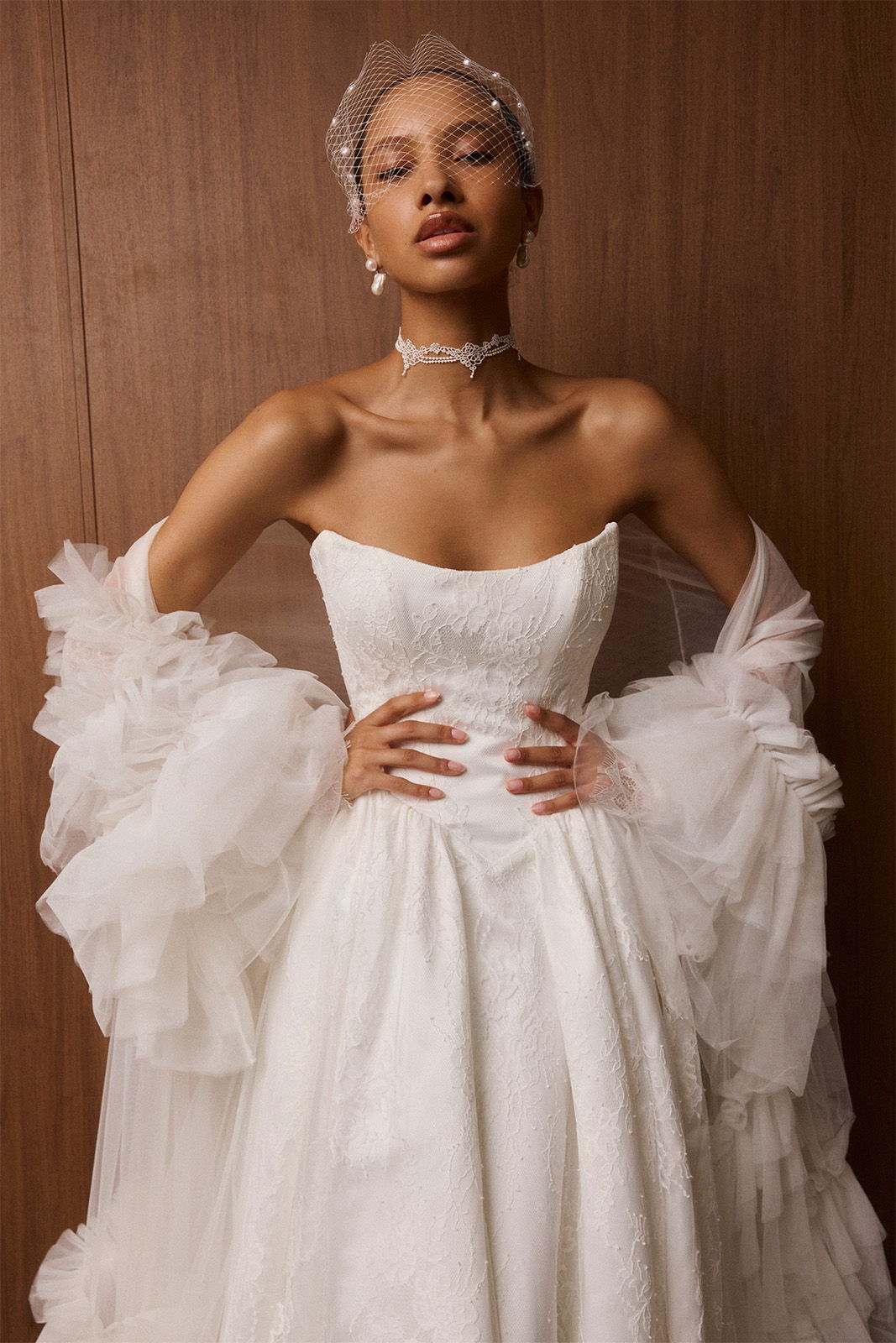 Model in a white wedding dress with dramatic sleeves, posing elegantly.