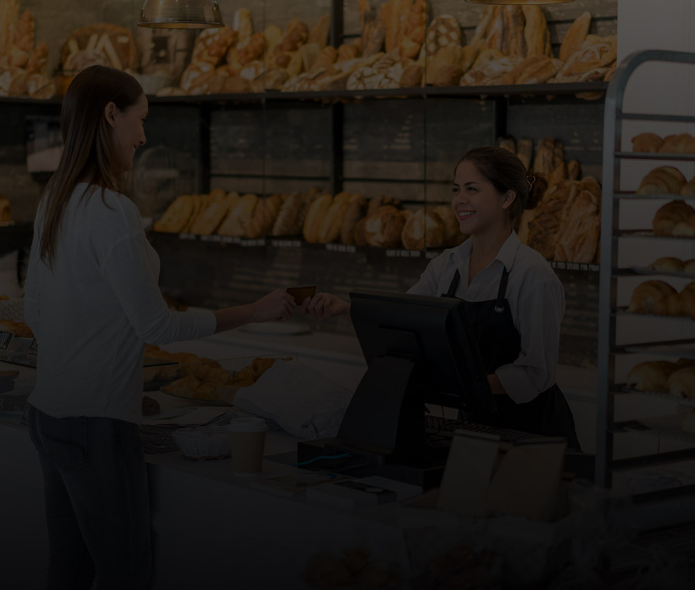 Bakery staff serving a customer at the counter, representing security and monitoring solutions for restaurants and food service businesses