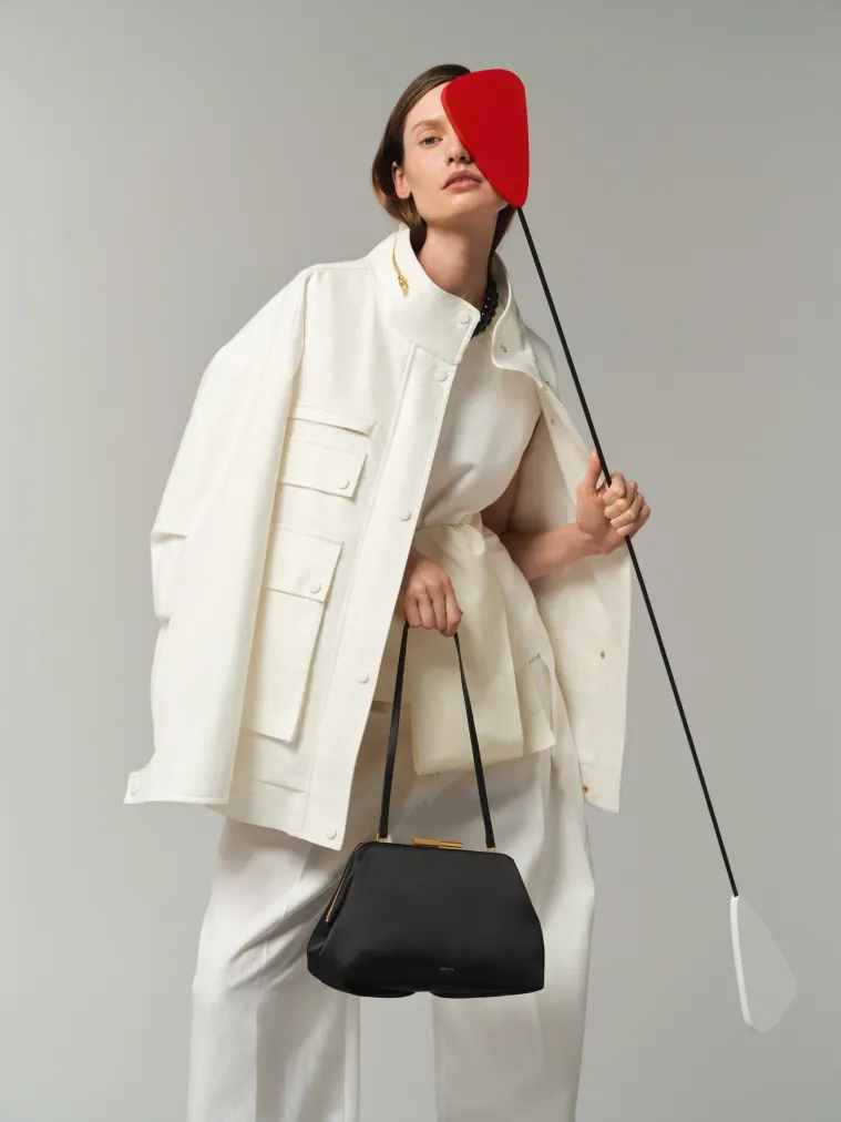 Model in a white outfit holding a black bag and a red object.