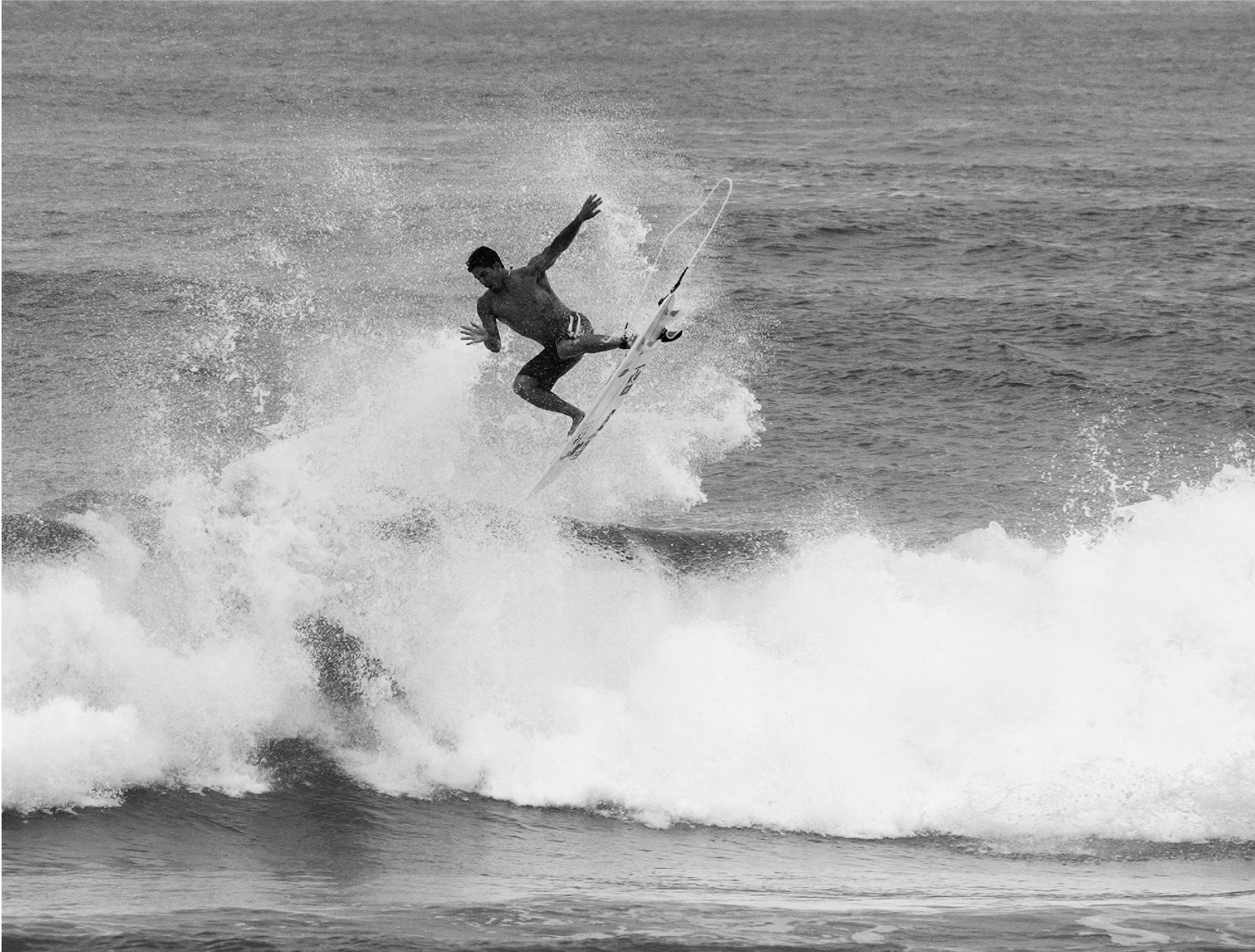 Un surfeur effectuant un saut au-dessus d'une vague, en noir et blanc.