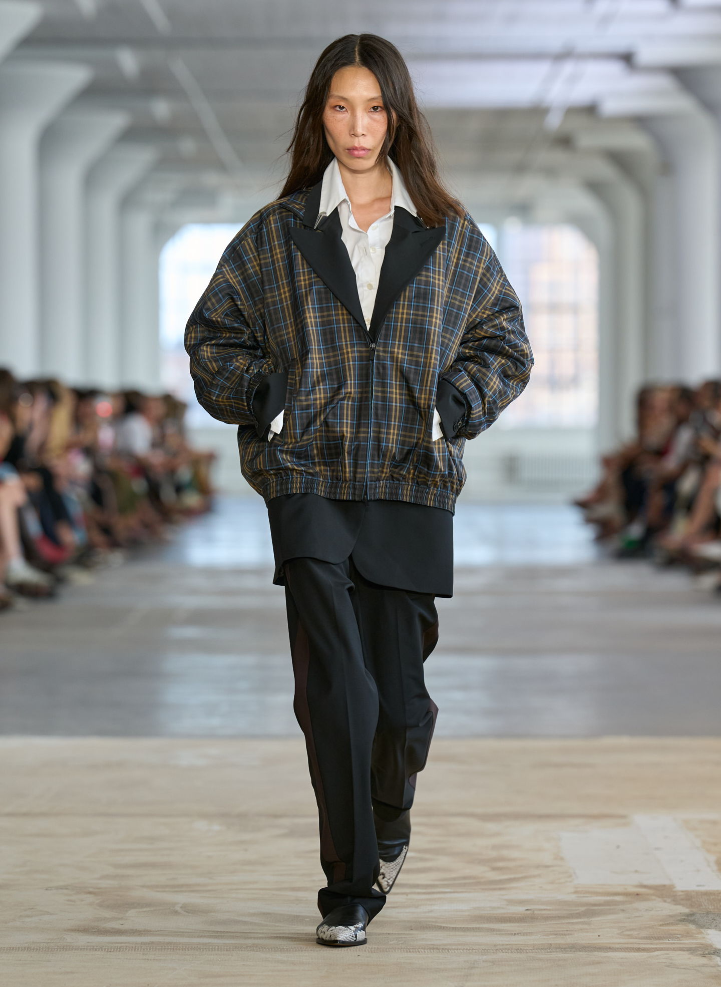 Model walking down runway in oversized jacket and black pants.