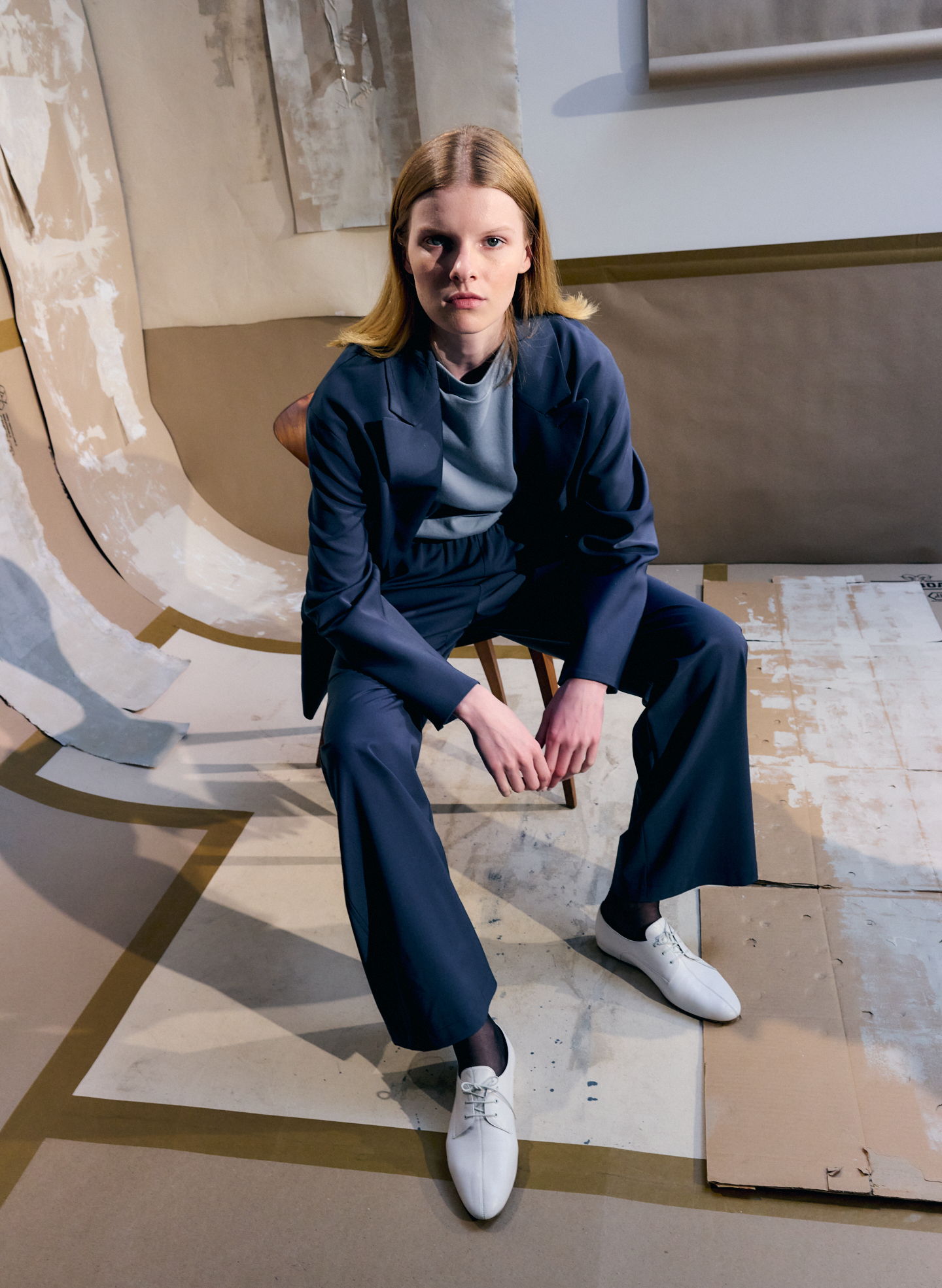 Model in navy outfit sitting on a chair in an artistic setting.