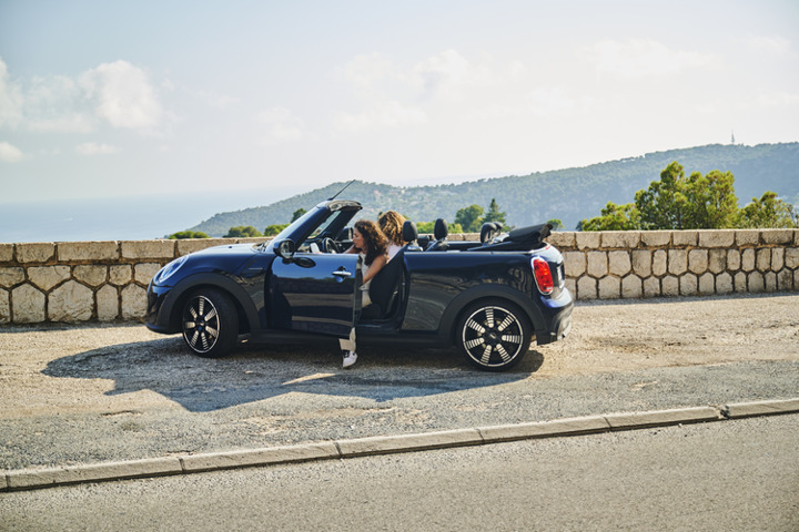 Person leaning on a blue convertible car by a scenic view.