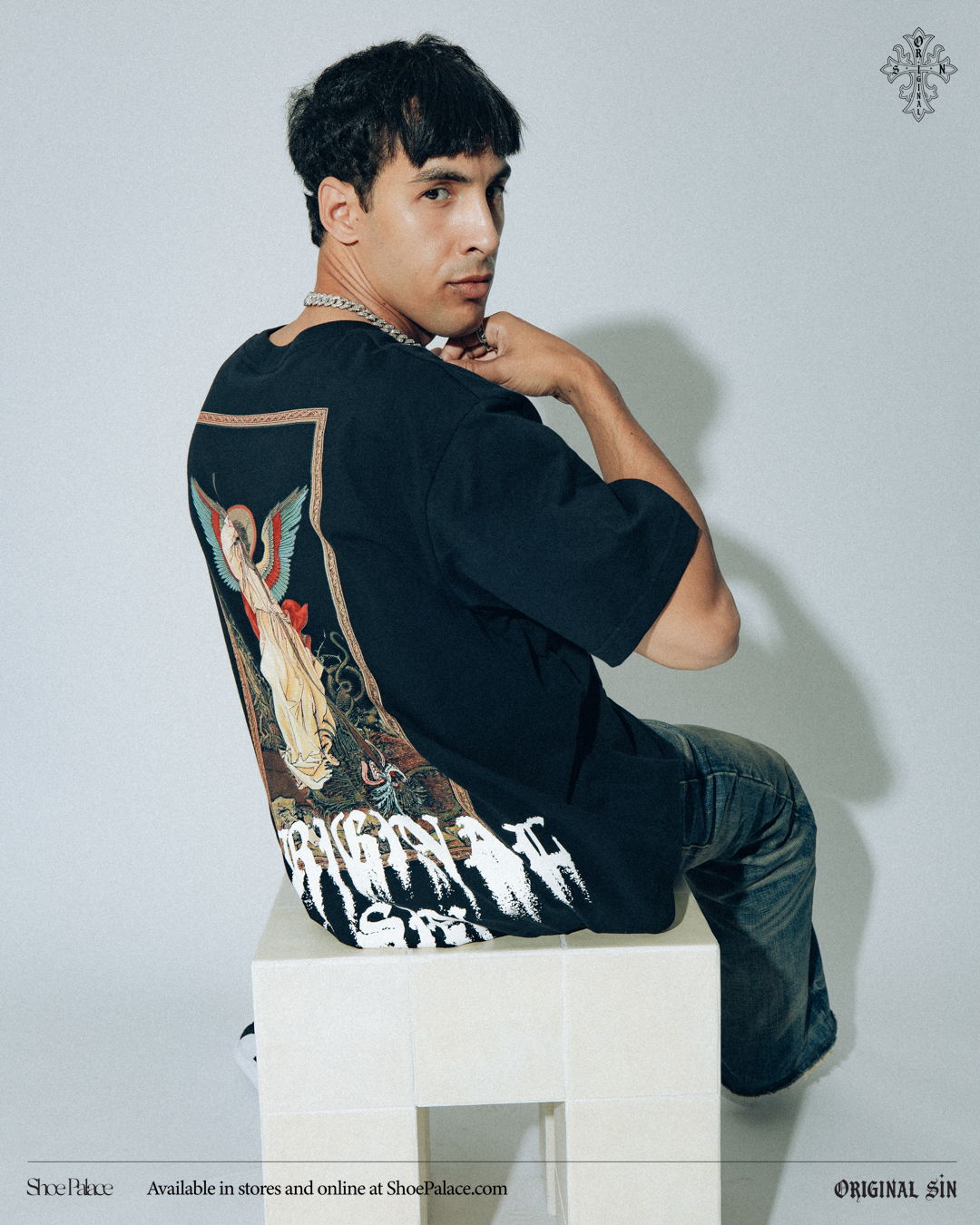 Person in a black shirt with graphic design, sitting on a white pedestal.