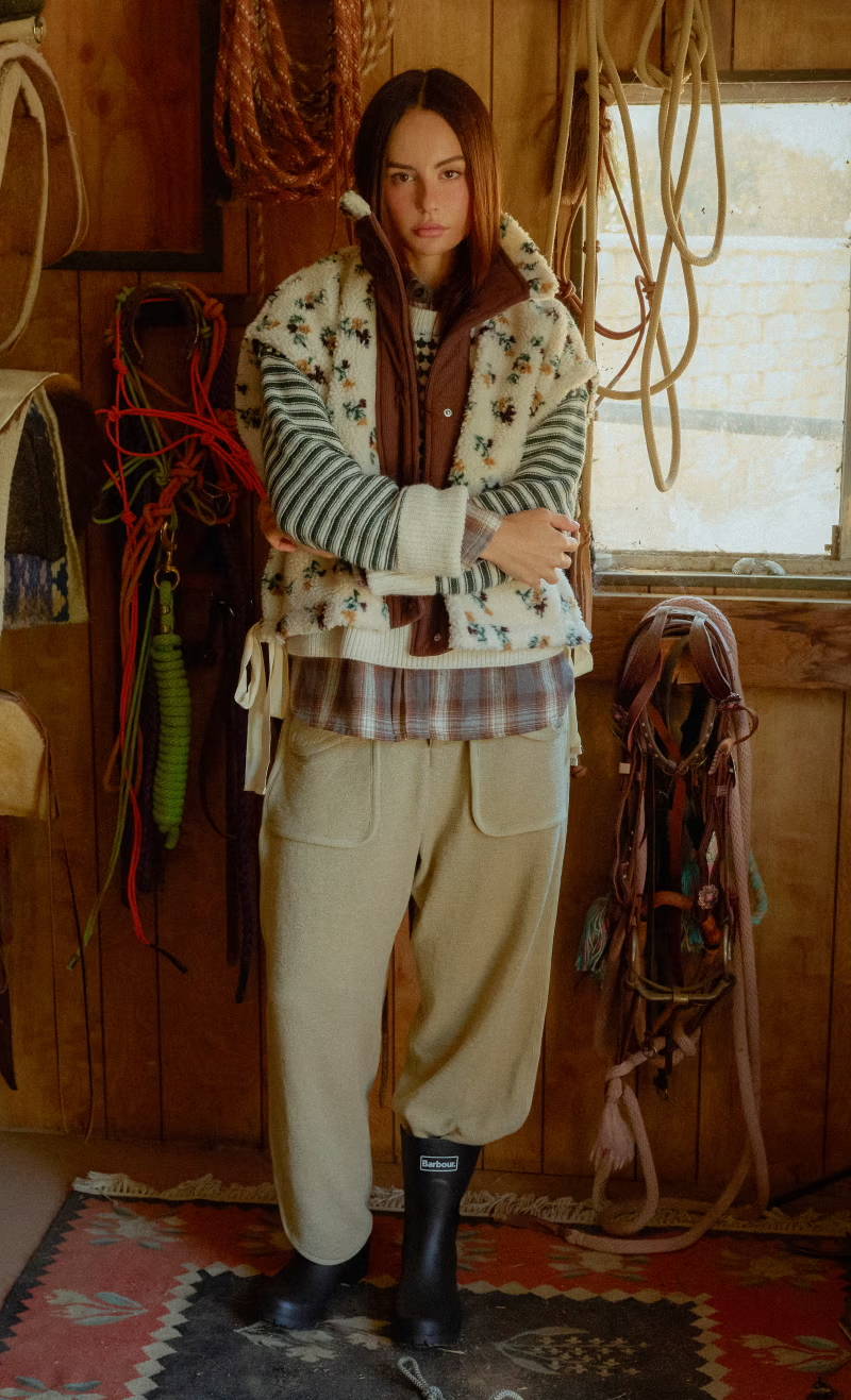 Person wearing layered clothing, standing in a rustic environment with ropes.