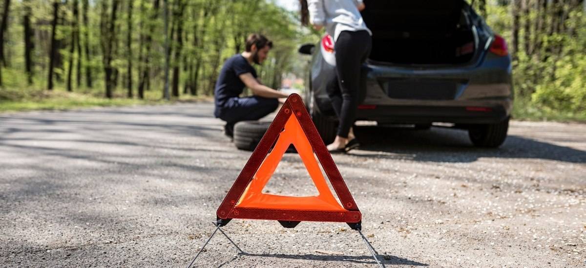 Reflective safety triangle from a car emergency kit being used while couple changes a flat tire on the side of the road