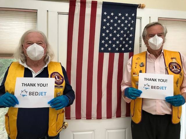 Two men in yellow vests wearing N95 masks hold signs that say 