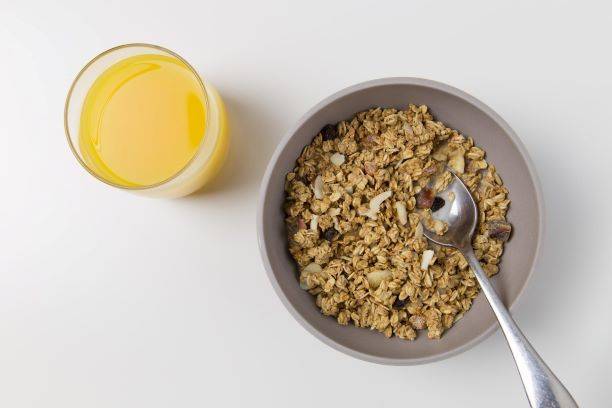 Oats And Nuts In Grey Bowl With A Glass Of Ornage Juice