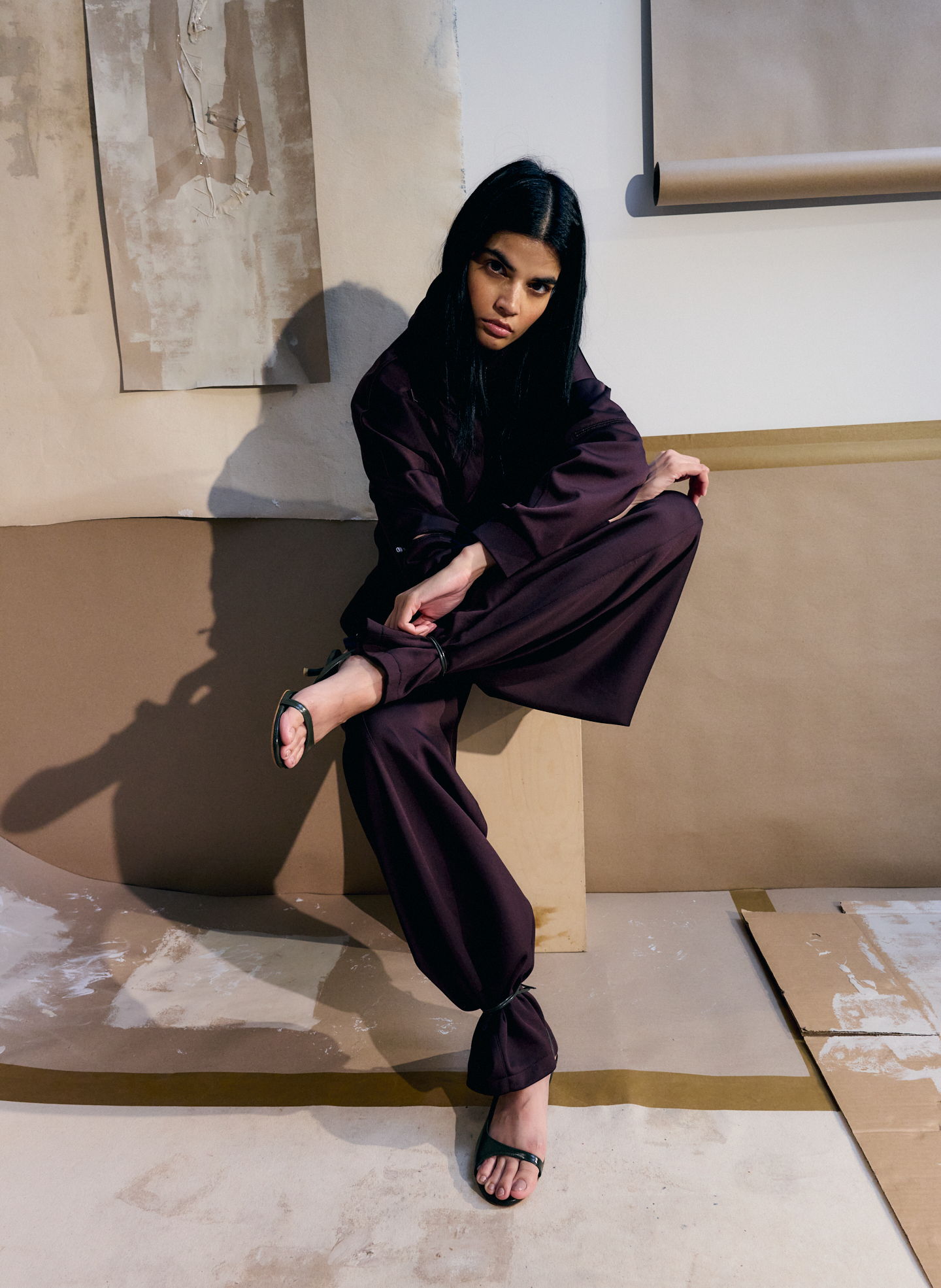 A model poses in stylish dark clothing against a minimalist backdrop.