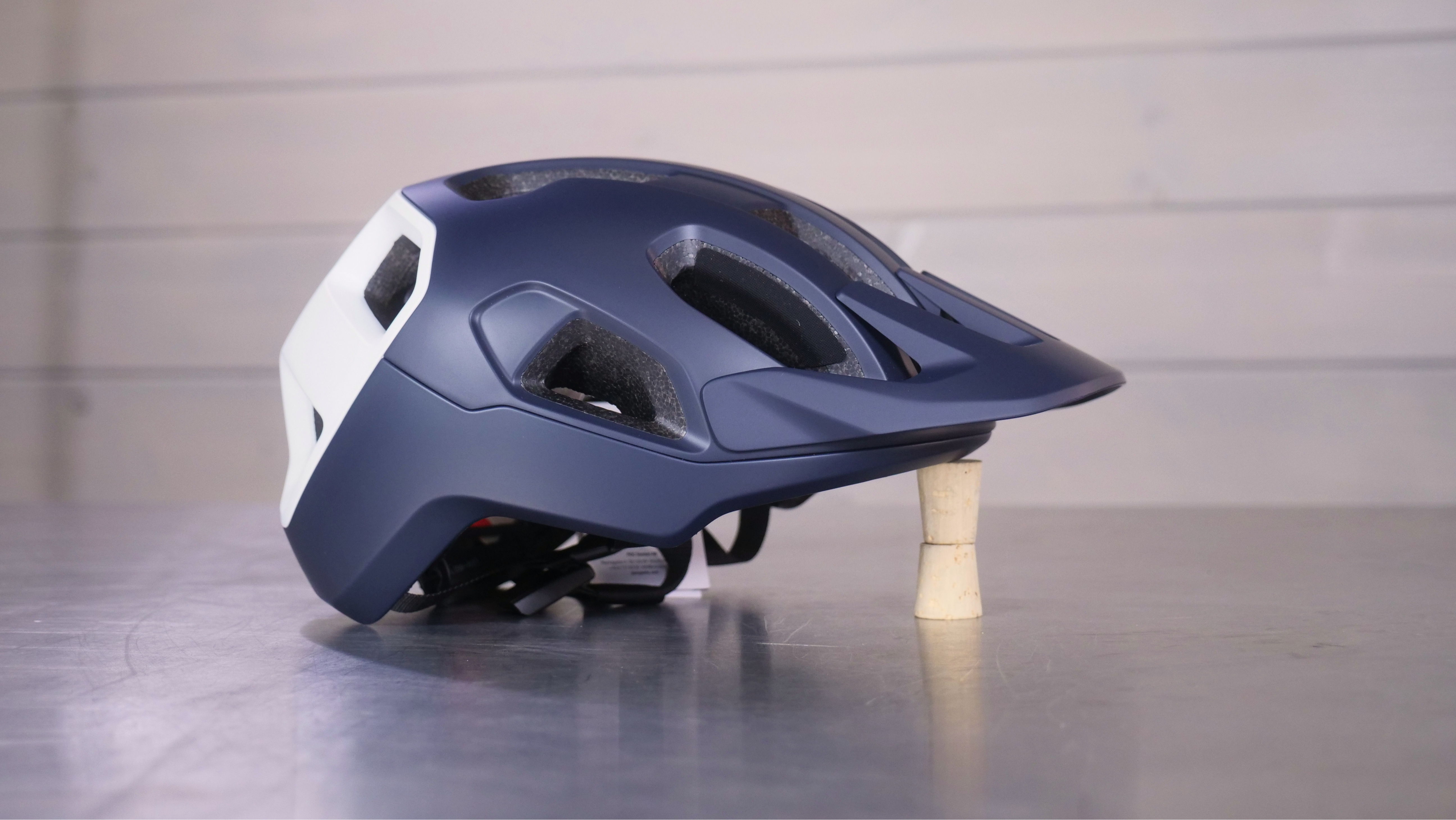 Navy blue bicycle helmet on a metal surface with a wooden block underneath.