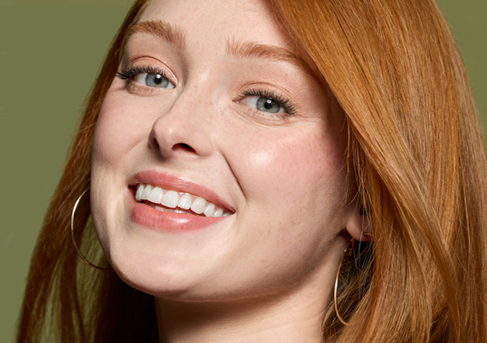 Smiling woman with red hair and earrings against a green background.
