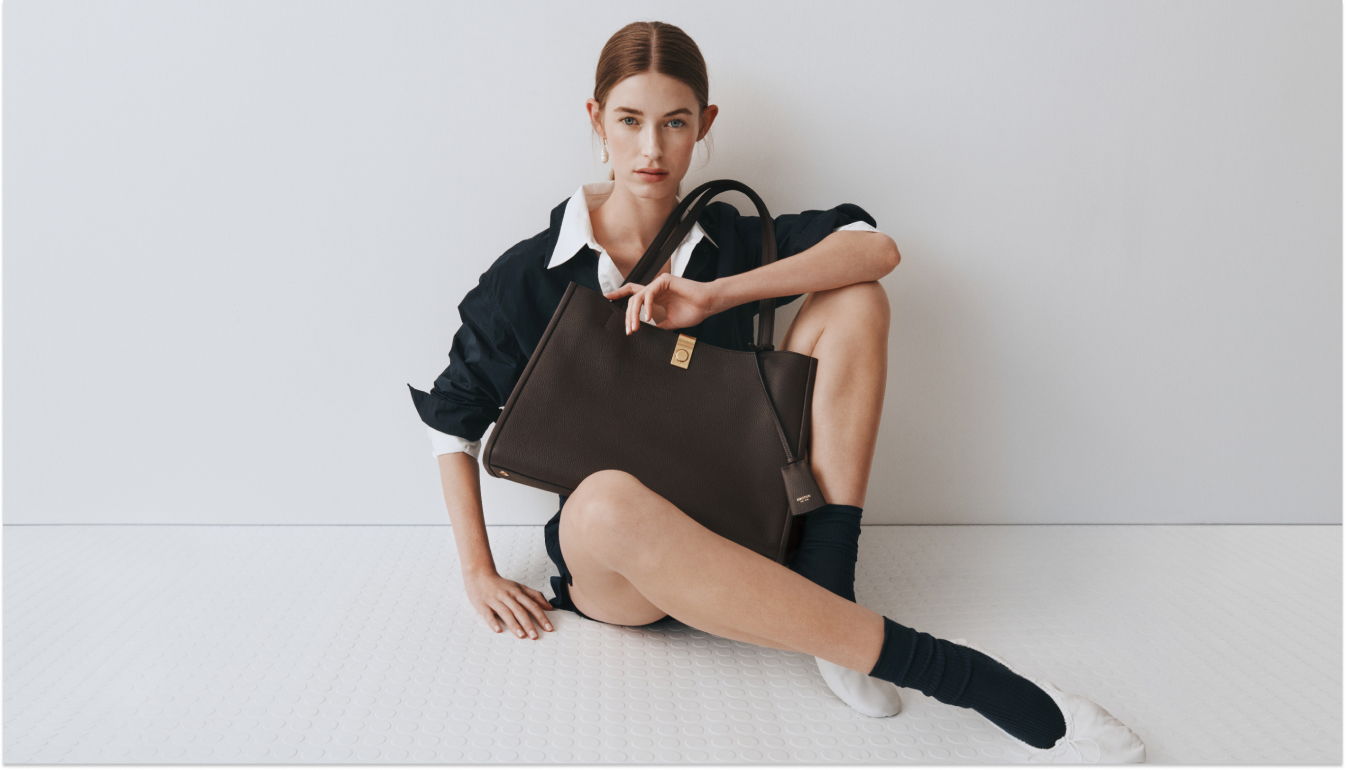 Young woman sitting with a brown handbag against a minimalist background.