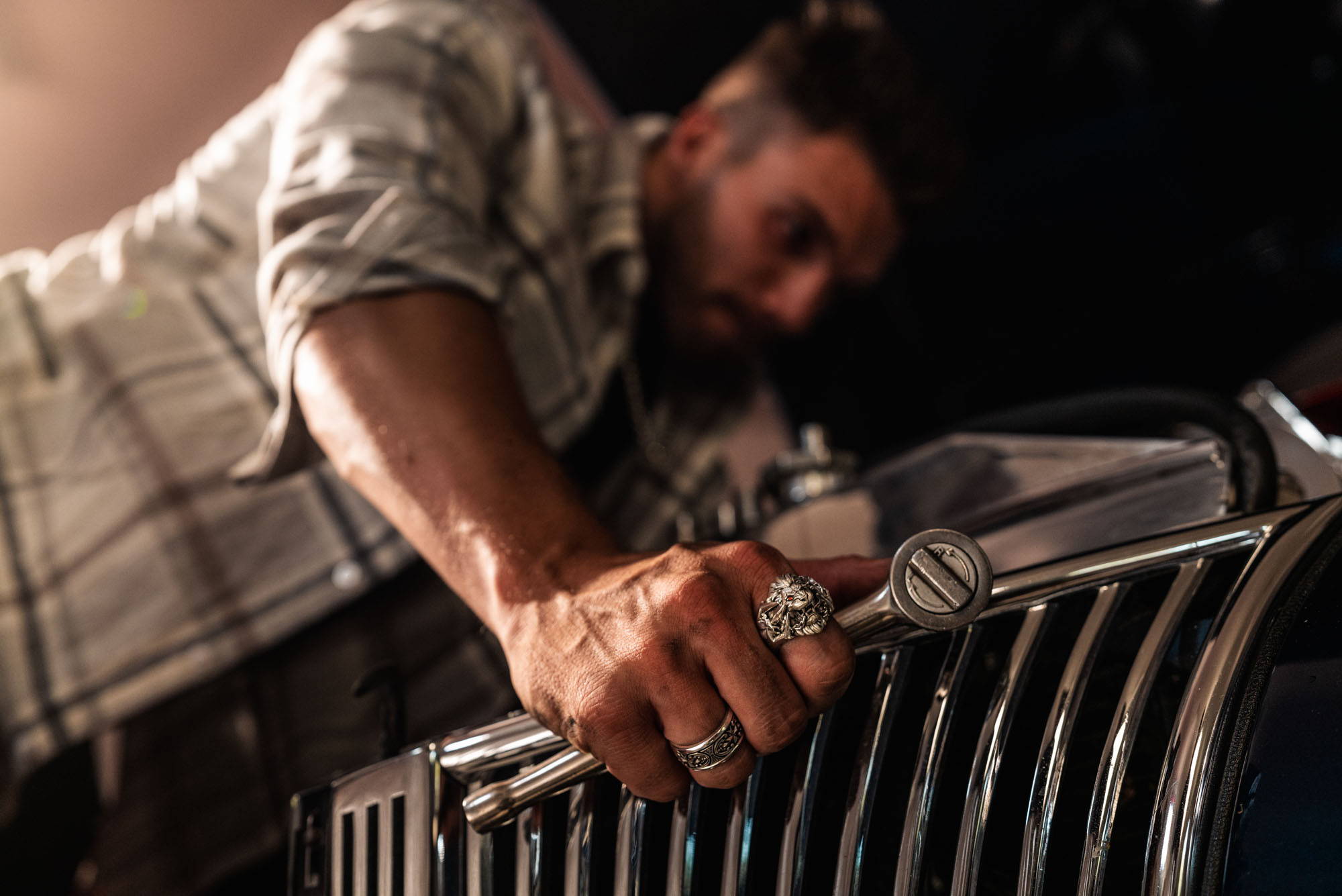 A man wearing a Rudiarius Band working under the hood of a classic car