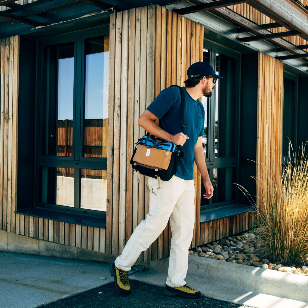 Man walking with a bag near a modern wooden building.