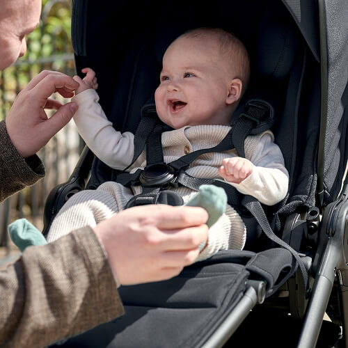 Happy baby in stroller reaching out to an adult.