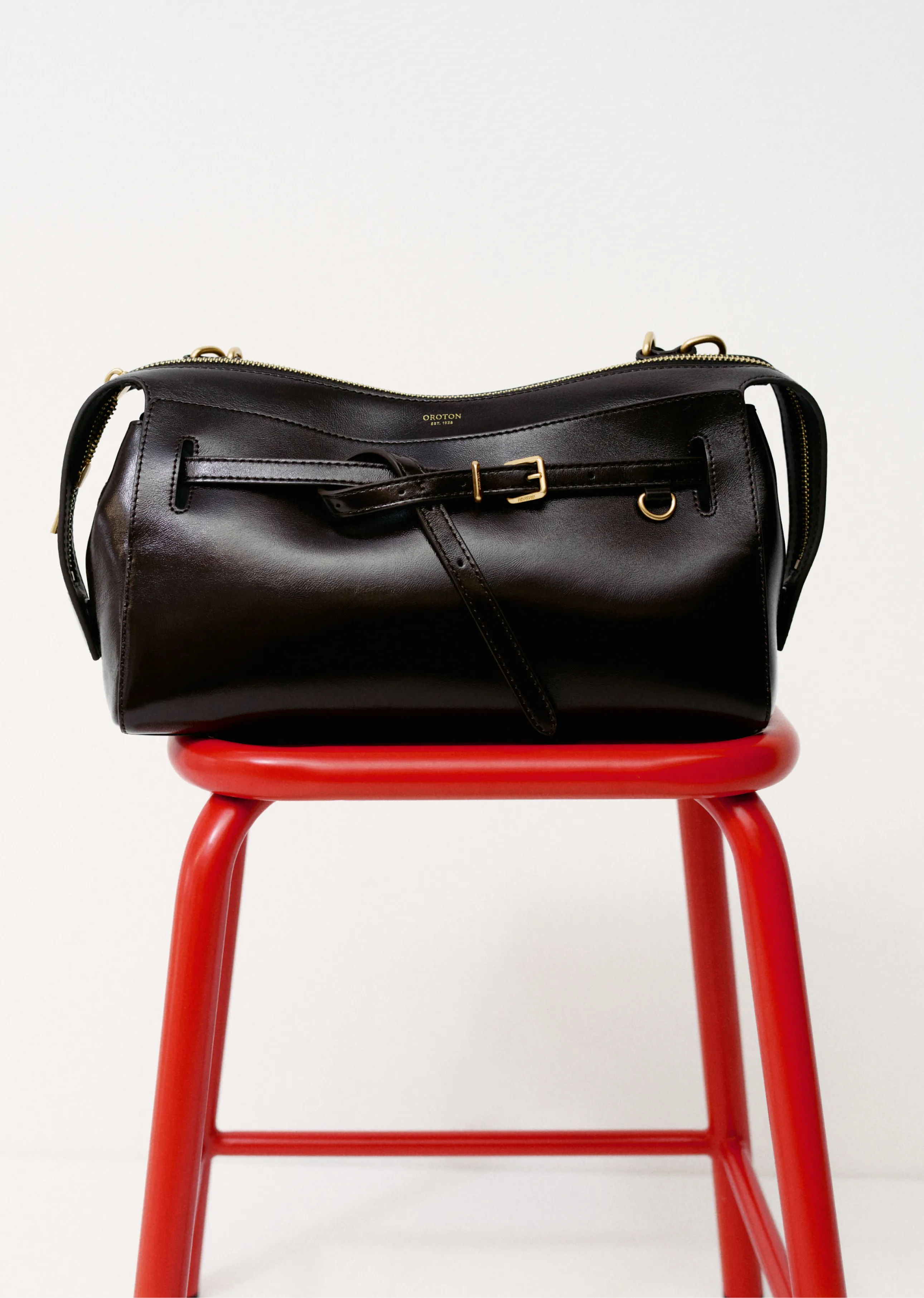 A black handbag resting on a red stool against a white background.