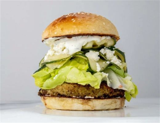 A burger with lettuce, pickles, and a sesame seed bun.
