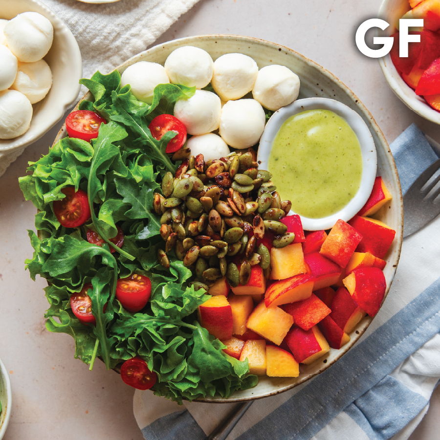A colorful salad with greens, tomatoes, fruit, nuts, and dressing. Gluten-free.